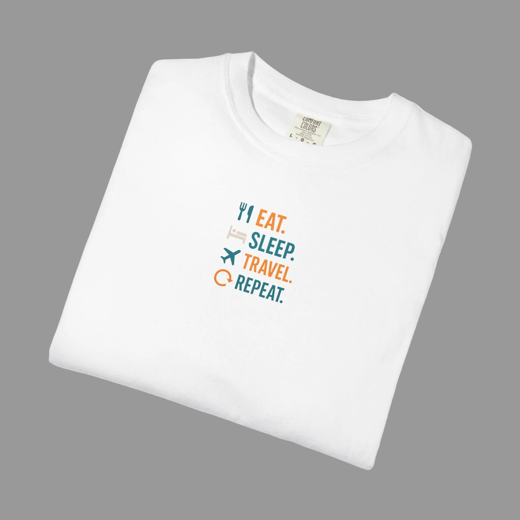 White t-shirt with 'Eat. Sleep. Travel. Repeat.' text and icons on a grey background