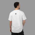 Person wearing a white t-shirt with a black and white logo on the back, standing against a shady background