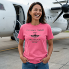 Woman wearing a pink t-shirt with an airplane graphic and text, standing in front of a propeller airplane.